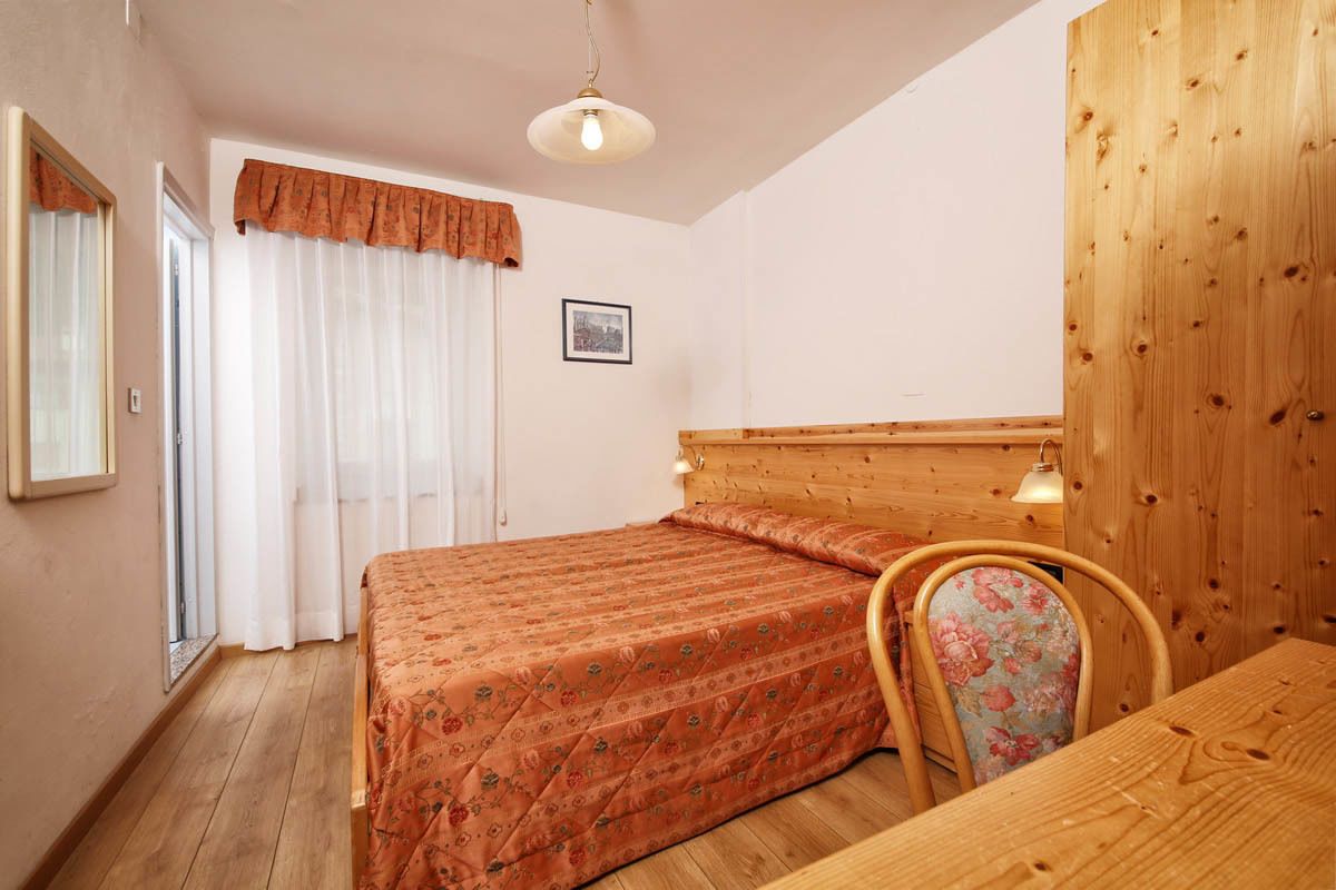A bedroom with a wooden bed, a chair, a table, and a window with curtains.