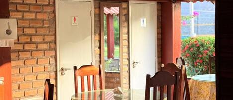A dining area with a round glass table, wooden chairs, a brick wall, and a door with a peephole.
