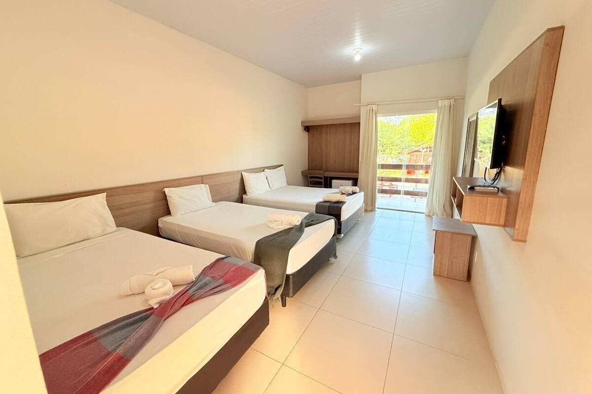 A hotel room with three beds, a TV, a desk, and a view of the outdoors.