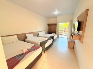 Habitación de hotel con tres camas, televisor, escritorio y vistas al exterior.