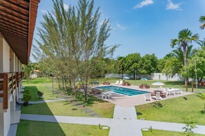 Una piscina con solárium, rodeada de mobiliario de exterior y árboles.