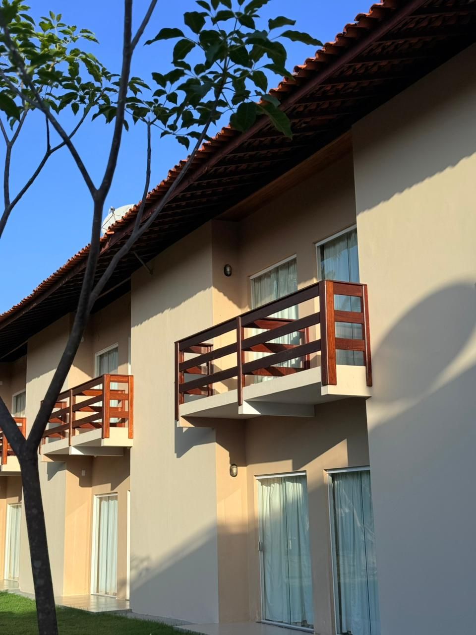 A multi-story building with balconies, windows with curtains, and a clear sky.