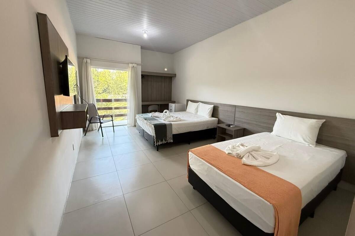 A hotel room with two beds, a desk, a chair, and a view of the outdoors.