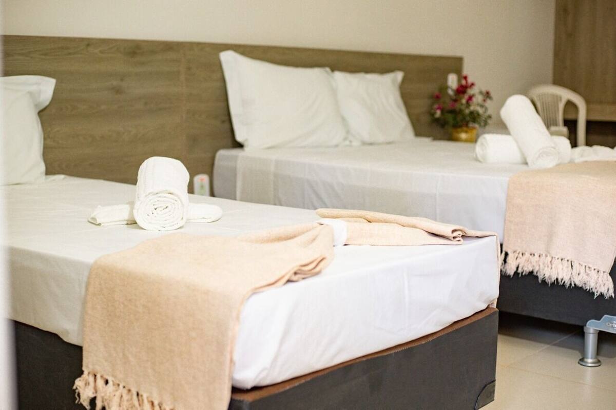 A hotel room with two beds, each with white linens and a beige blanket.