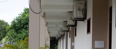 Een gang met airconditioningunits, potplanten en een schone betegelde vloer.