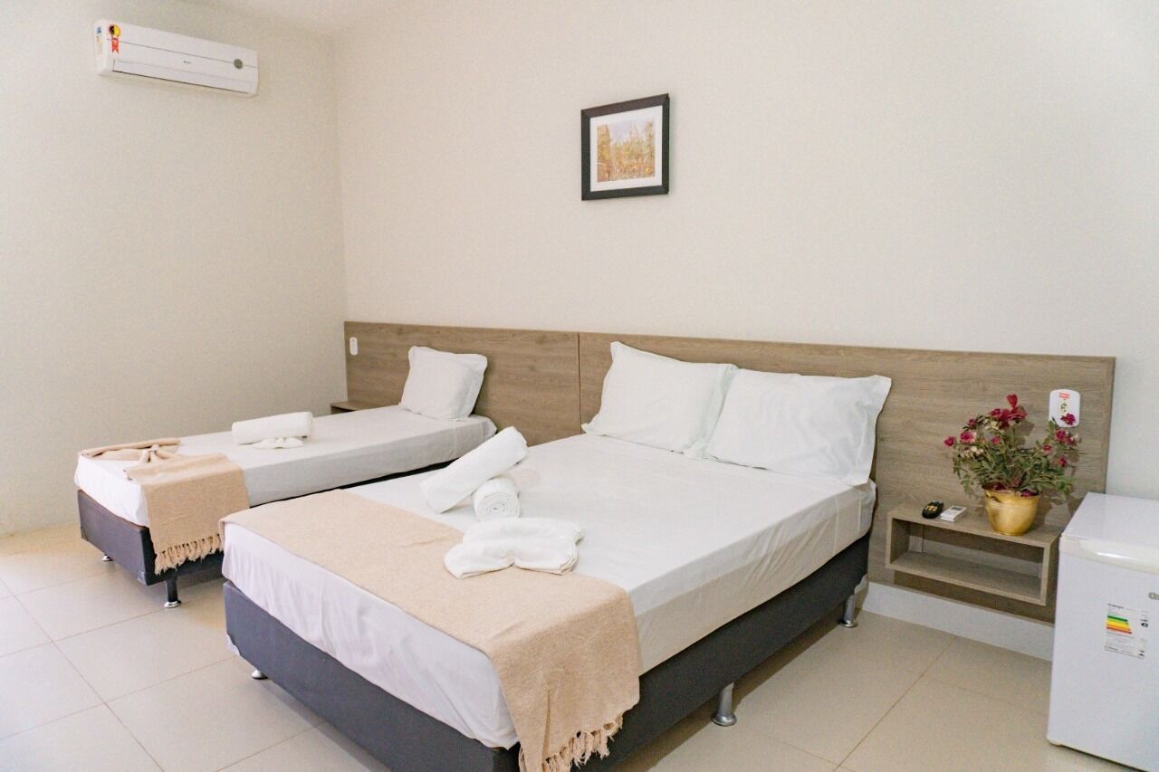 Habitación de hotel con dos camas individuales, una mesita de noche con una planta y un aire acondicionado instalado en la pared.