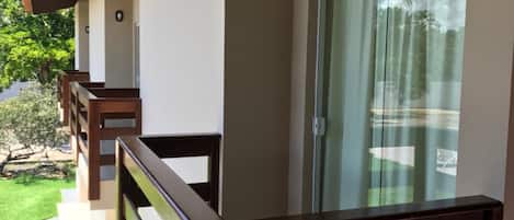 A balcony with a wooden railing, a sliding glass door, and a view of a green lawn.