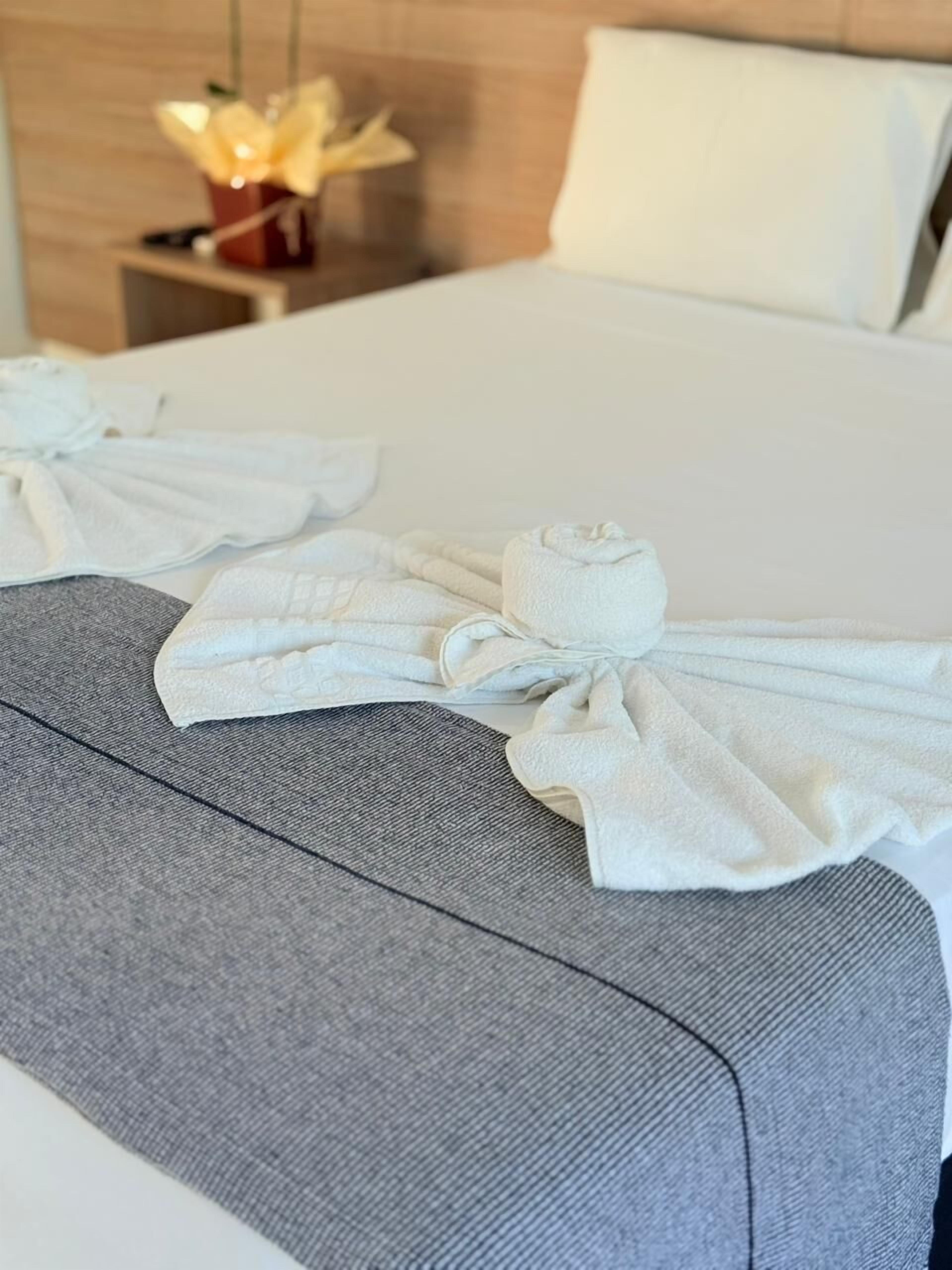 Cama bem arrumada com lençóis brancos e cabeceira estofada cinza.