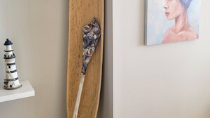 A wooden surfboard leaning against a wall, a small shelf with a lighthouse model, and a painting of a woman. - Edificio Marina del Rey (Cartagena)