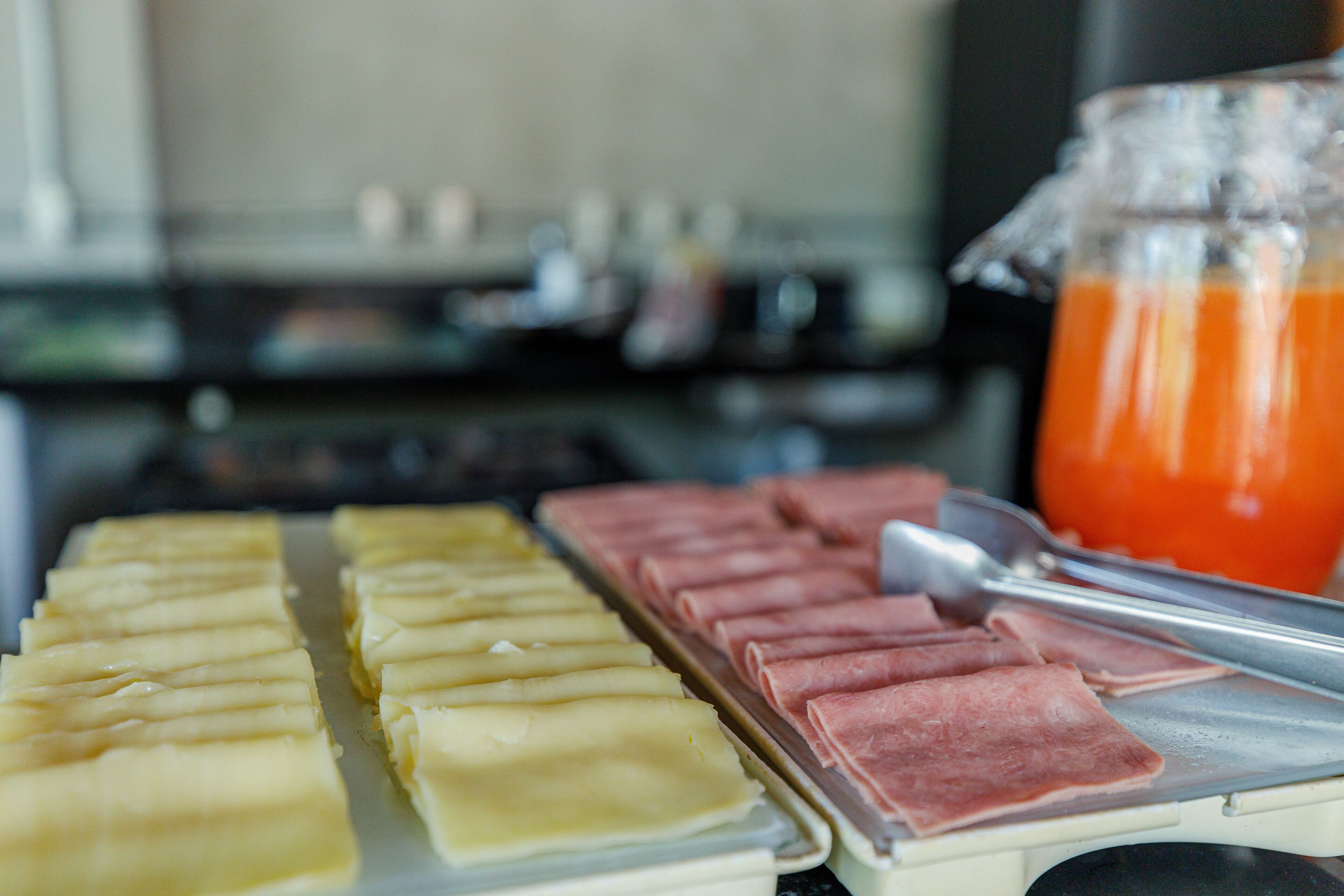 Uma bandeja com alimentos organizados, incluindo fatias amarelas e rosa, e um recipiente de vidro com líquido vermelho.