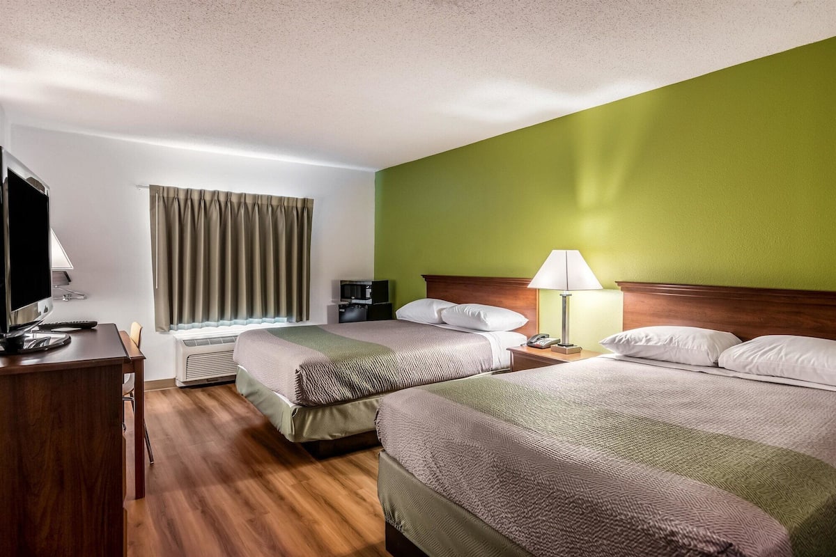 Habitación de hotel con dos camas, un escritorio con computadora, televisor y lámpara.