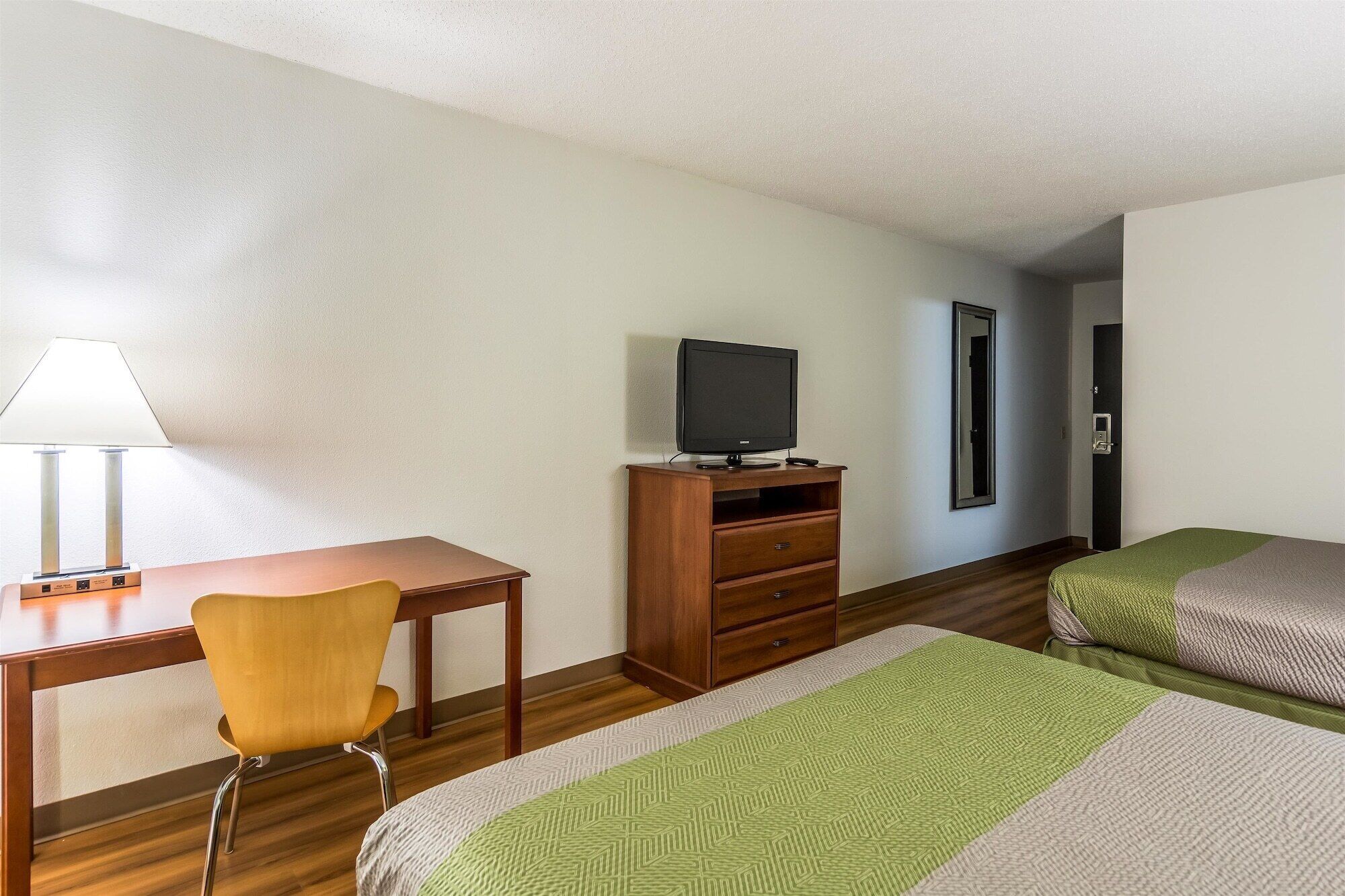 A hotel room with a desk, chair, television, and two beds.