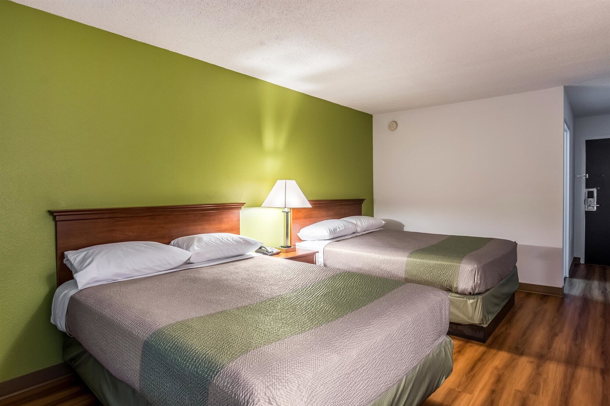 Une chambre d’hôtel avec deux lits, une table de chevet avec une lampe et une porte sur le côté droit.