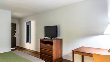 A hotel room with a bed, a wooden dresser with a television, a desk, and a chair.