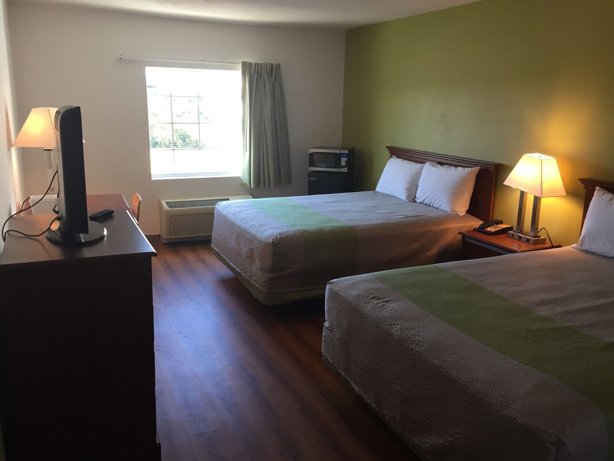 A hotel room with two beds, a desk with a computer, a TV, and a window with curtains.
