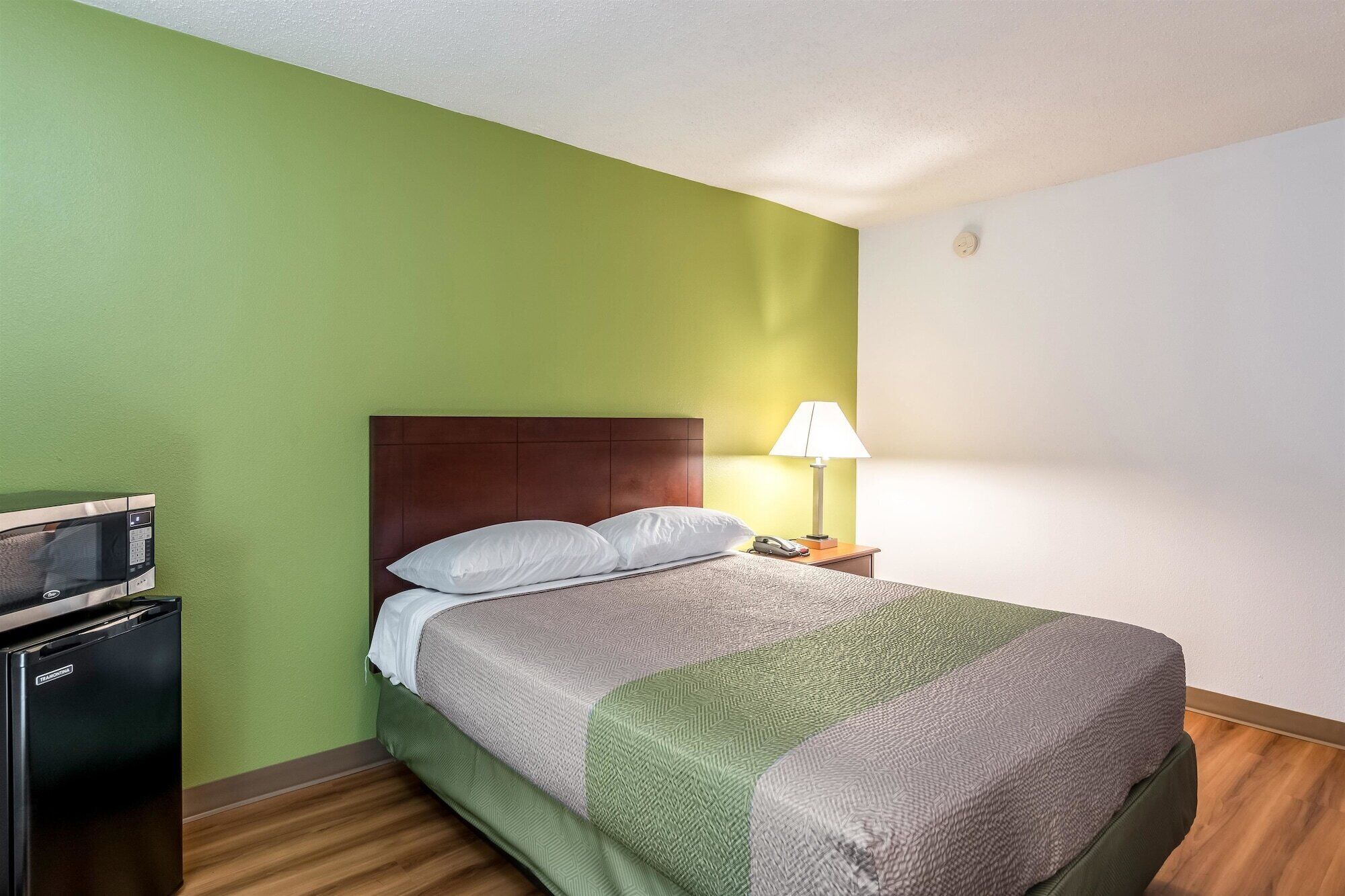 Une chambre d’hôtel équipée d’un lit, d’une table de chevet, d’une lampe, d’un four à micro-ondes et d’un réfrigérateur.