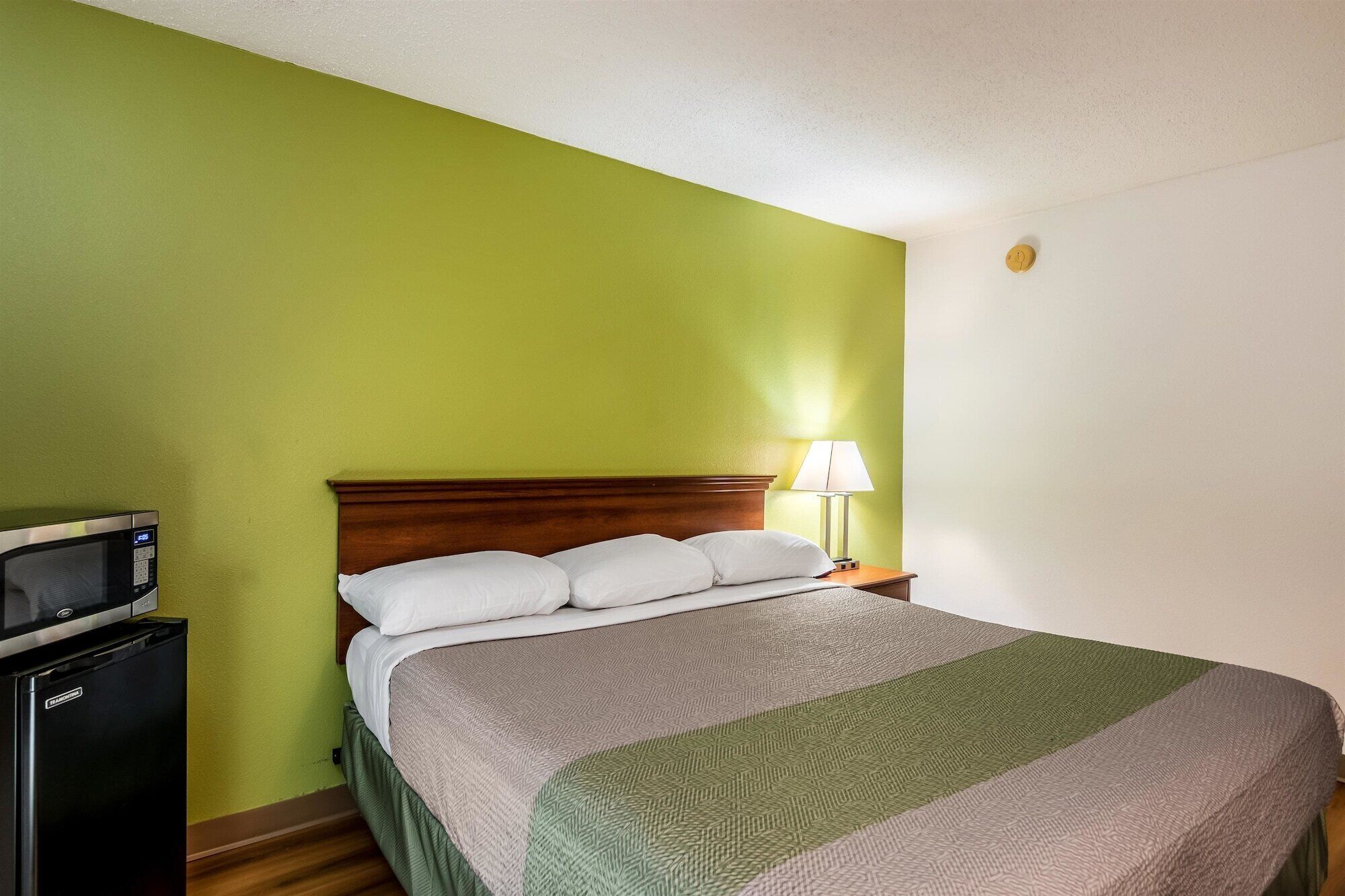 A hotel room with a bed, a nightstand, a lamp, and a microwave.