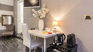 A hotel room with a white table, a vase of white flowers, a lamp, a coffee maker, and a television on the wall. - Trastevere Sweet House (Rome)