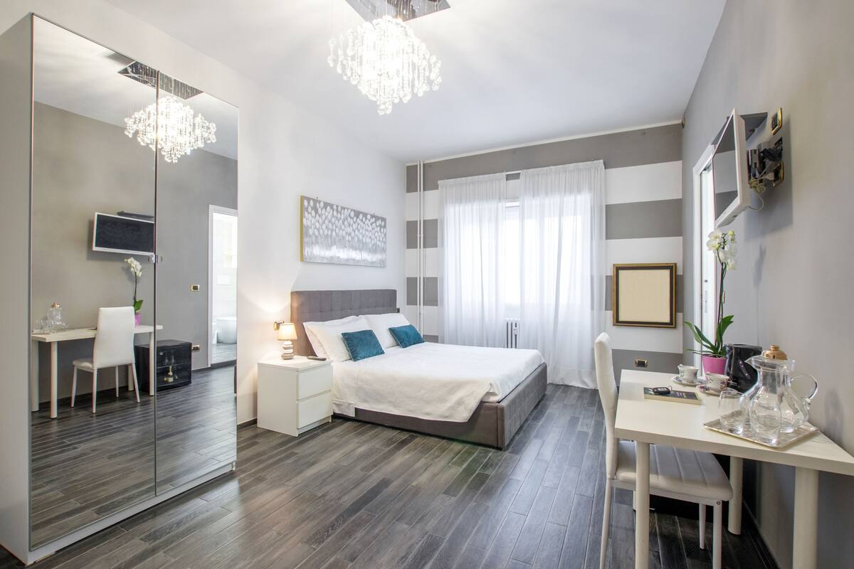 A modern bedroom with a large bed, bedside tables, a desk, and a mirror.