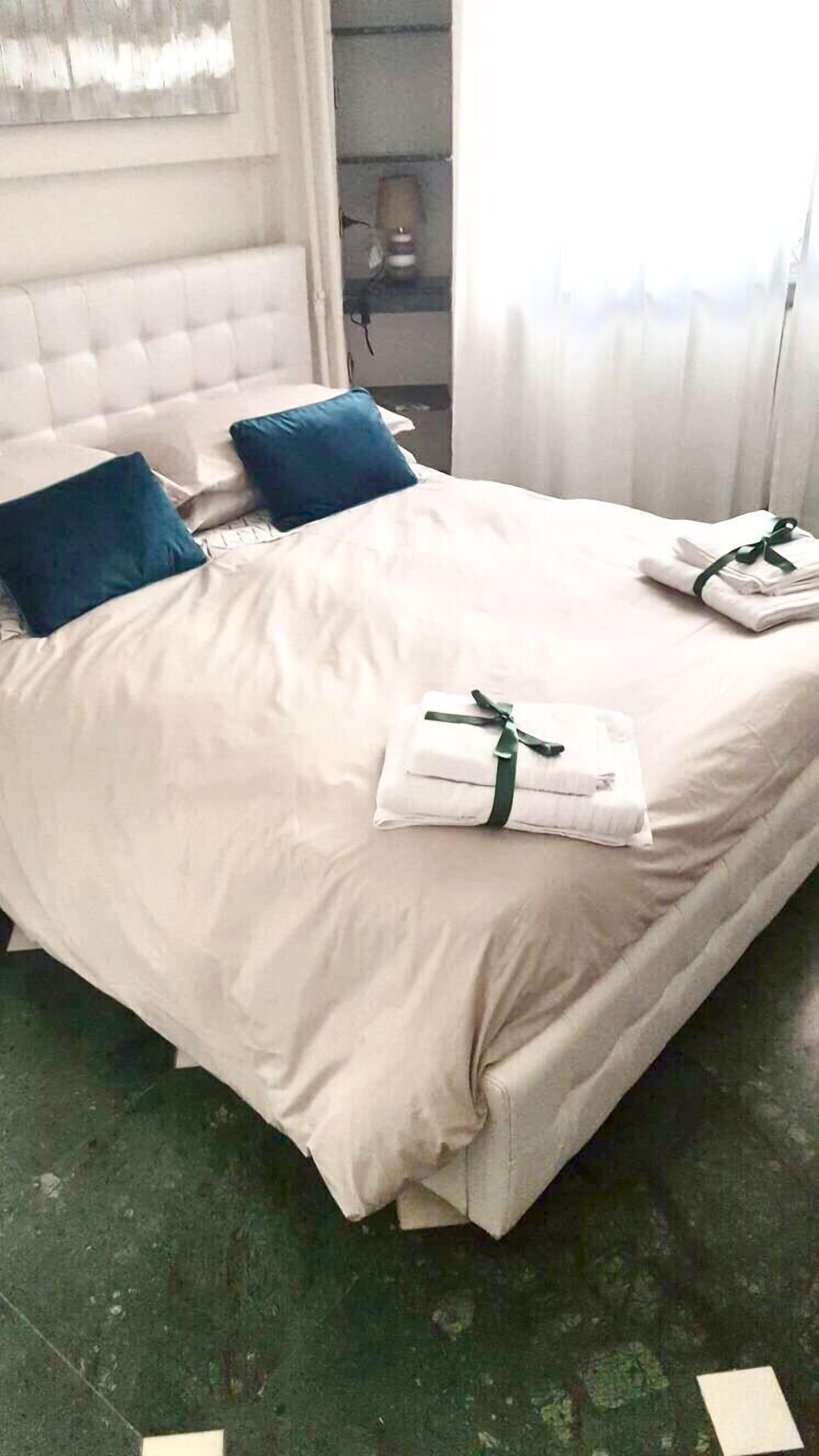 A neatly made bed with pillows, a folded towel, and a small card on the floor.