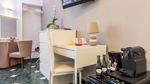 A hotel room with a desk, chair, and a coffee machine. There is a TV mounted on the wall, a small table with a lamp, and a plant. - Trastevere Sweet House (Rome)