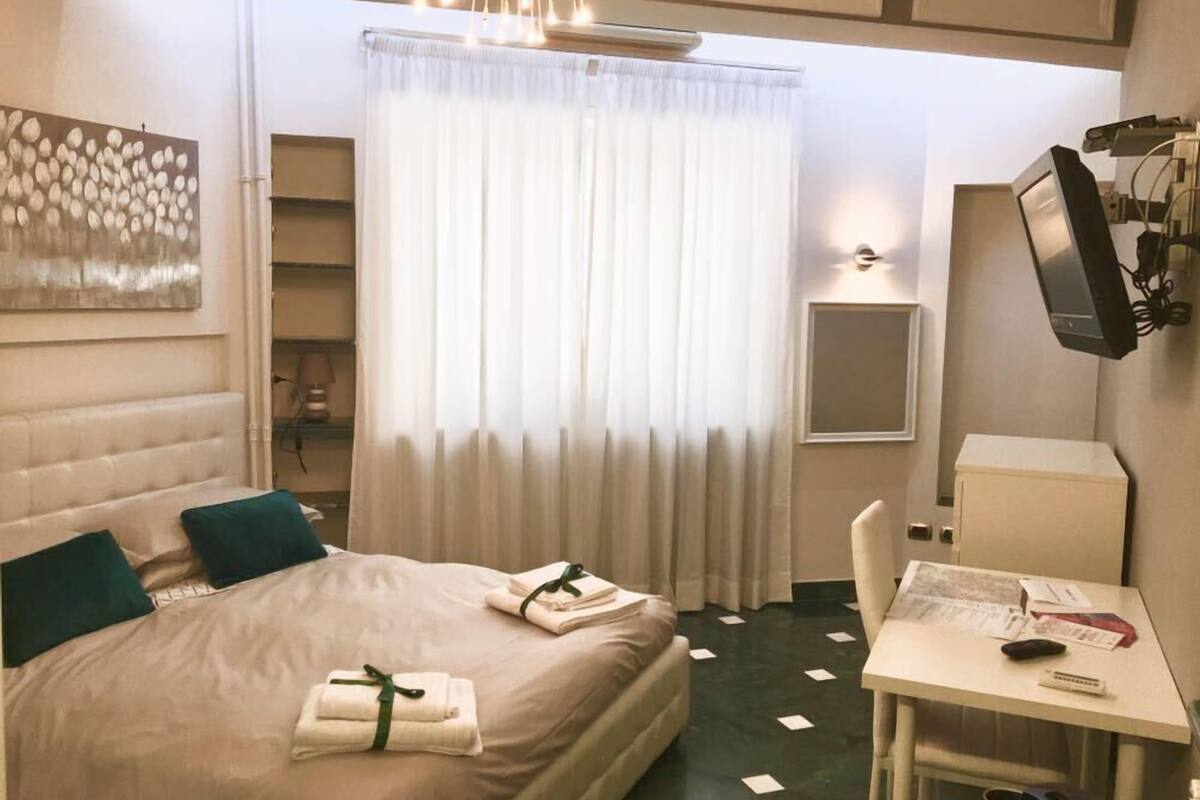 A hotel room with a bed, a desk, a TV, and a window with curtains.
