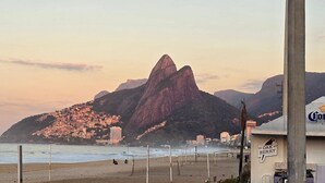 A beach with a prominent mountain in the background, a sign for "Oak Berry," and a view of the ocean. - Rio Spot Begossi (Rio de Janeiro)