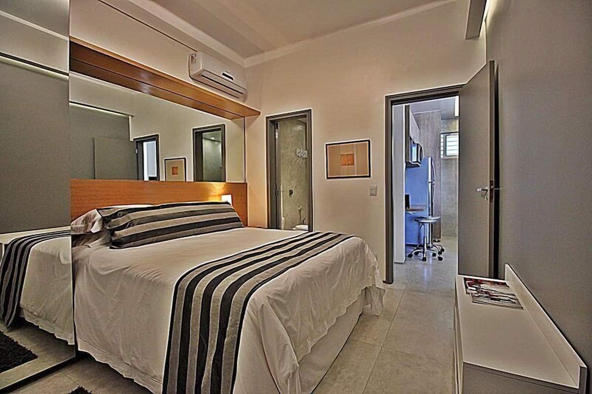 A modern bedroom with a large bed, a mirror, and a door leading to a bathroom.
