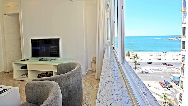 A modern hotel room with a large window offering a view of the beach and ocean. - Rio Spot Begossi (Rio de Janeiro)