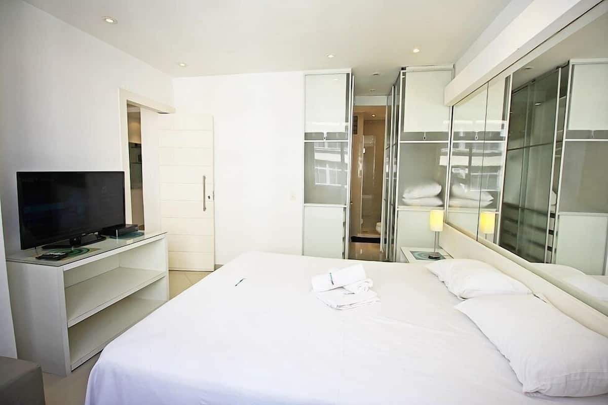 A hotel room with a bed, a TV on a stand, a wardrobe, and a bathroom with a glass door.