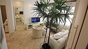 A modern living room with a large potted plant, a flat-screen TV, a white sofa, and a glass coffee table. - Rio Spot Begossi (Rio de Janeiro)