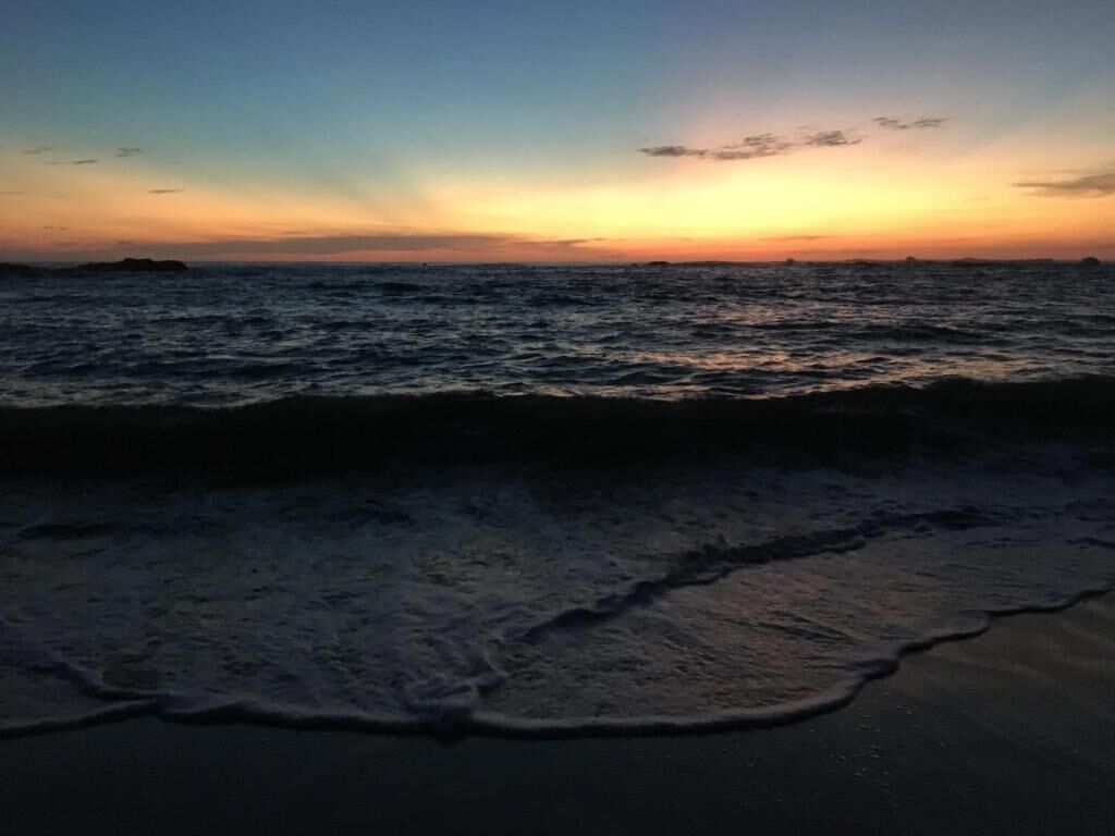 A beach at sunset with waves approaching the shore.