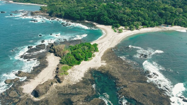 Luchtbeeld van een kustgebied met strand, rotsachtige kustlijn en dicht bos.
