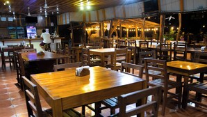 Een restaurant met houten tafels en stoelen, een bar en een plafondventilator.