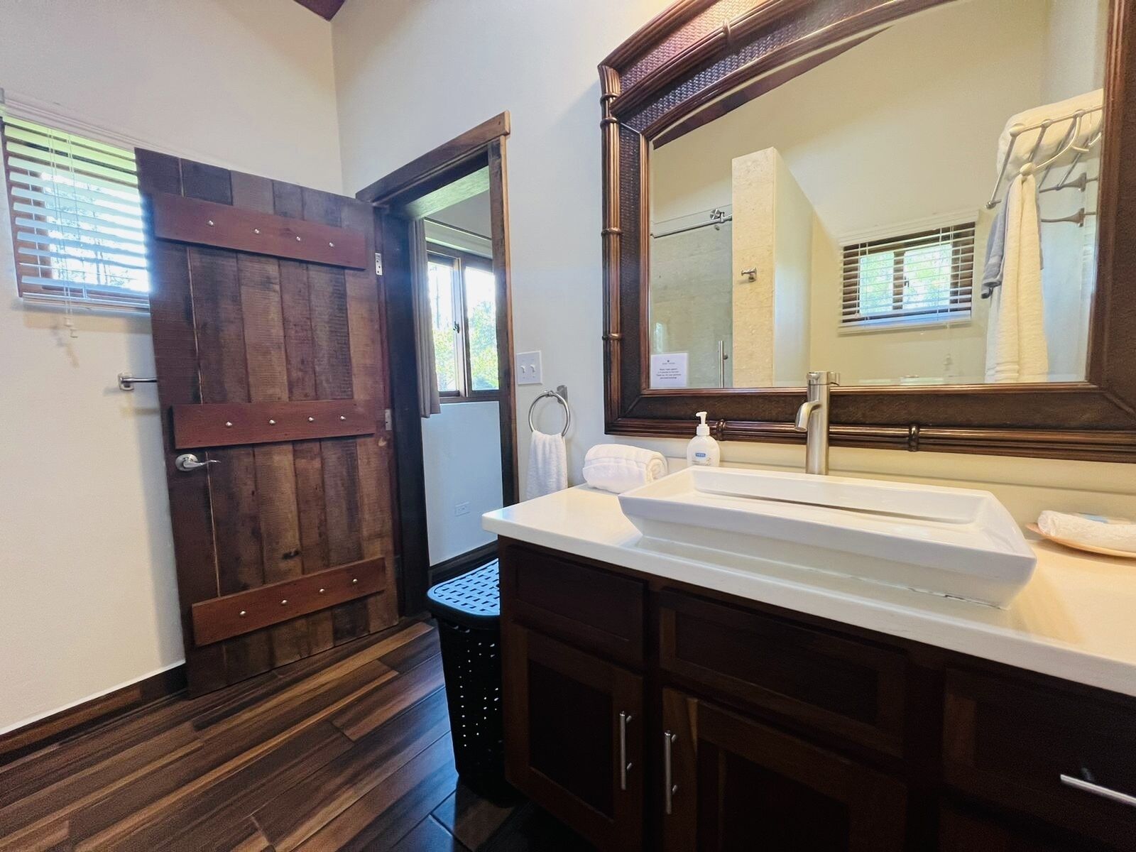 Un baño con puerta de madera, un espejo grande, un lavamanos y un perchero para toallas.