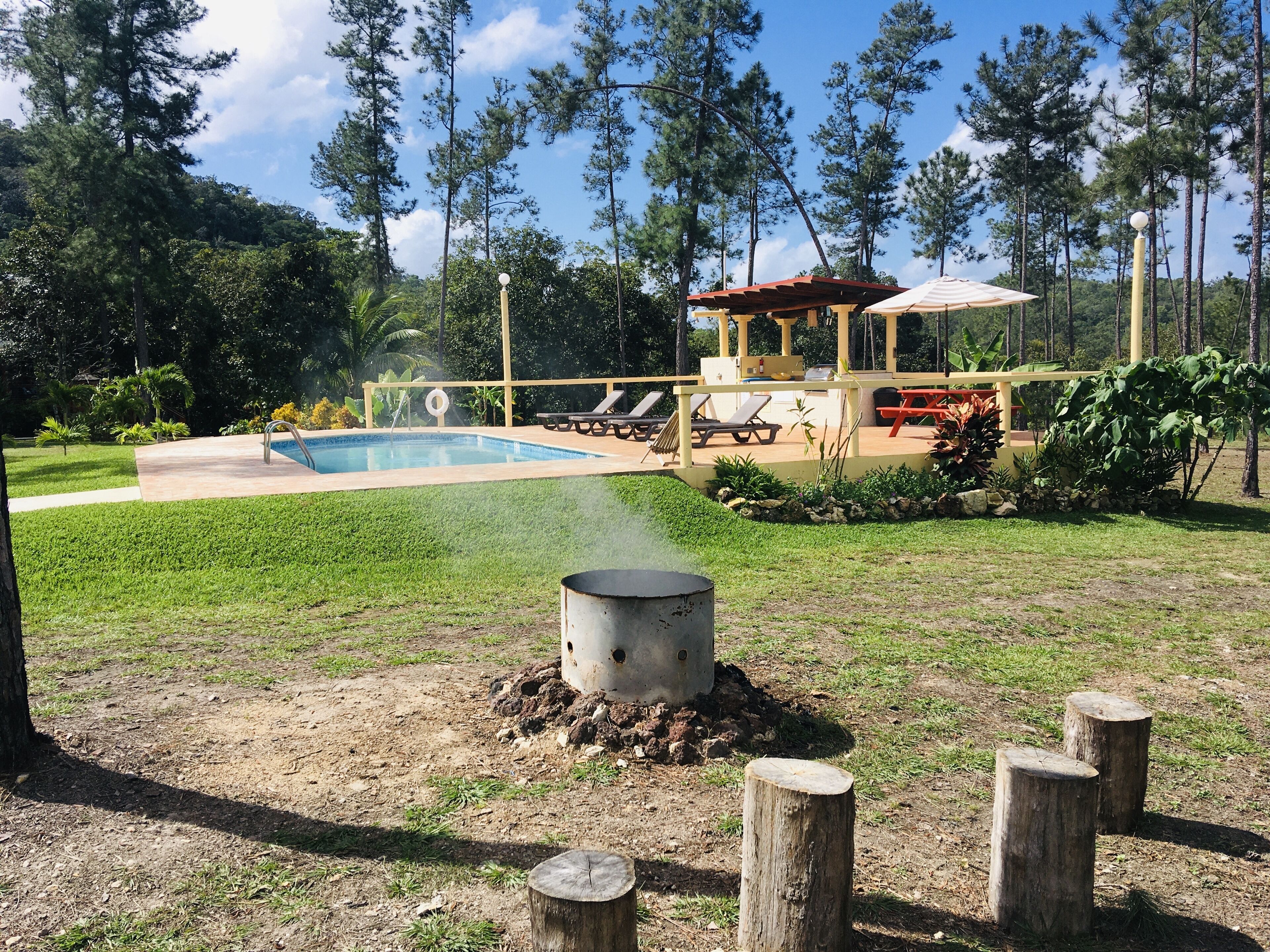 Un área de piscina con sillas de descanso, un espacio de estar cubierto y una chimenea.