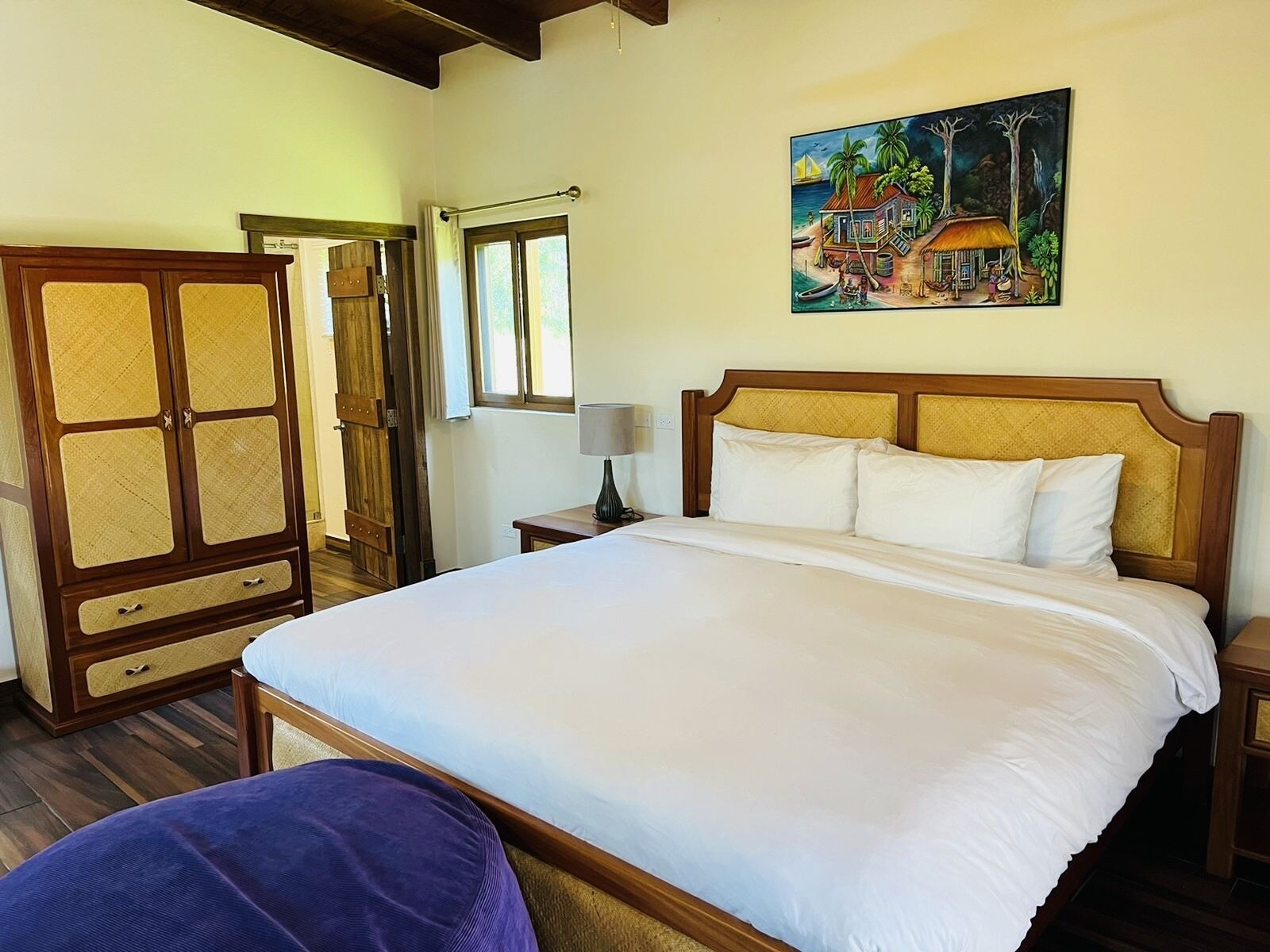 A bedroom with a large bed, wooden wardrobe, and a painting of a tropical scene.