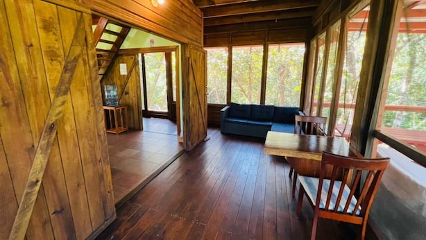 Un interior de madera con una zona de comedor, un sofá y una escalera que lleva a un nivel superior.