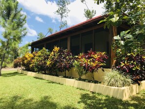 A building with a red roof and large windows, surrounded by a well-maintained garden with various shrubs and trees. - Kāne Villas (Mountain Pine Ridge)