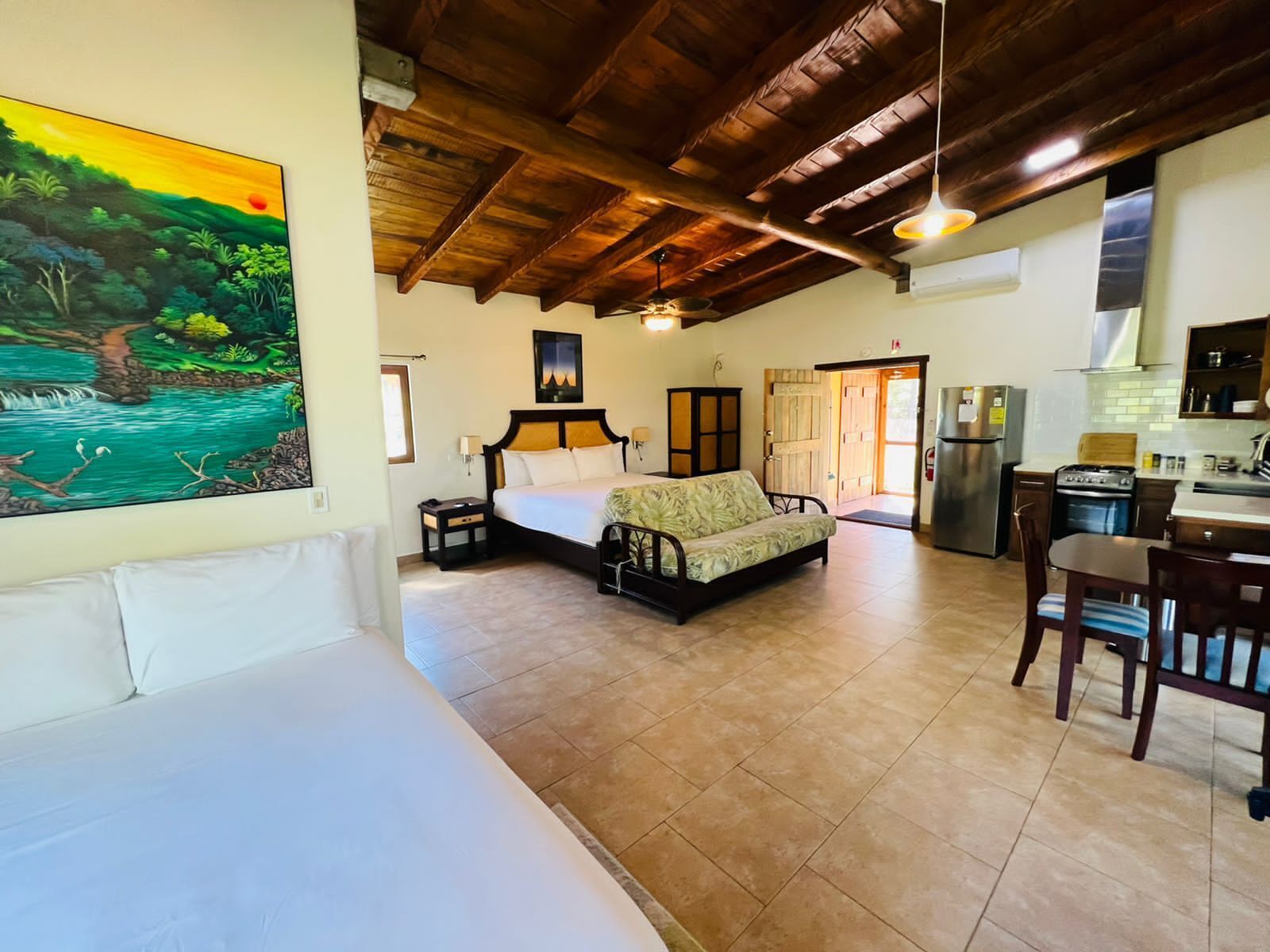 A spacious room with a bed, a sofa, a dining table, and a kitchen area.