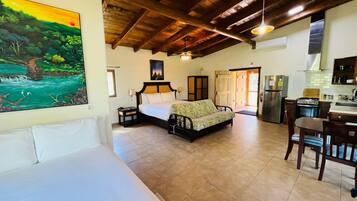 A spacious room with a bed, a sofa, a dining table, and a kitchen area.