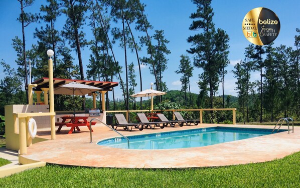 A pool area with lounge chairs, a barbecue station, and a covered seating area. - Kāne Villas (Mountain Pine Ridge)