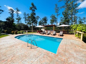 A swimming pool with lounge chairs and umbrellas, surrounded by trees. - Kāne Villas (Mountain Pine Ridge)