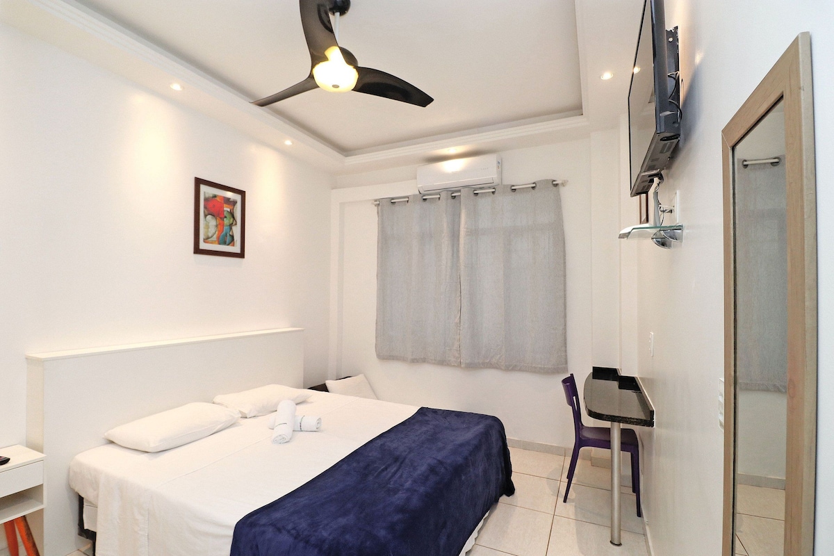 Une chambre à coucher comprenant un lit, un bureau, une chaise, un ventilateur de plafond et un appareil de climatisation.