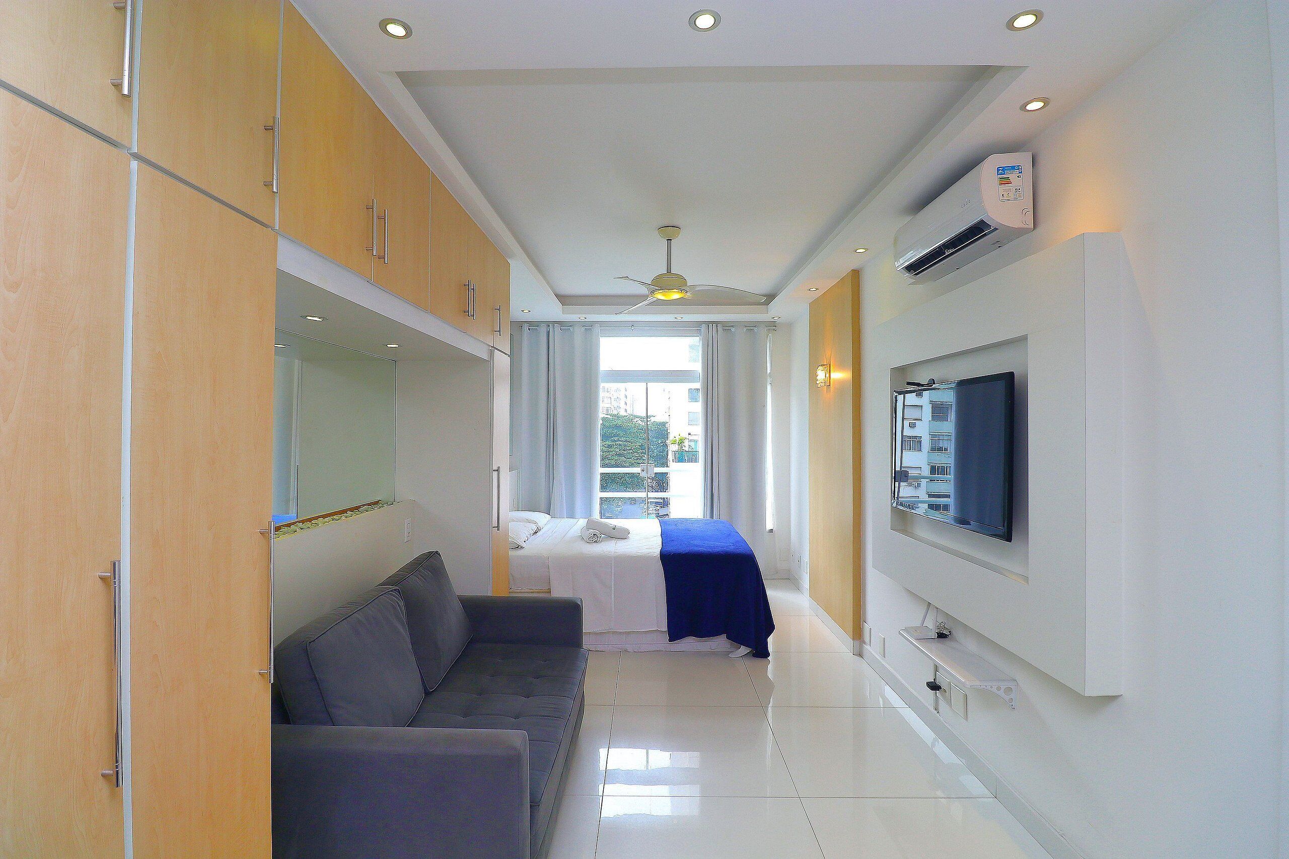 A modern hotel room with a sofa, a bed, a TV mounted on the wall, and a ceiling fan.