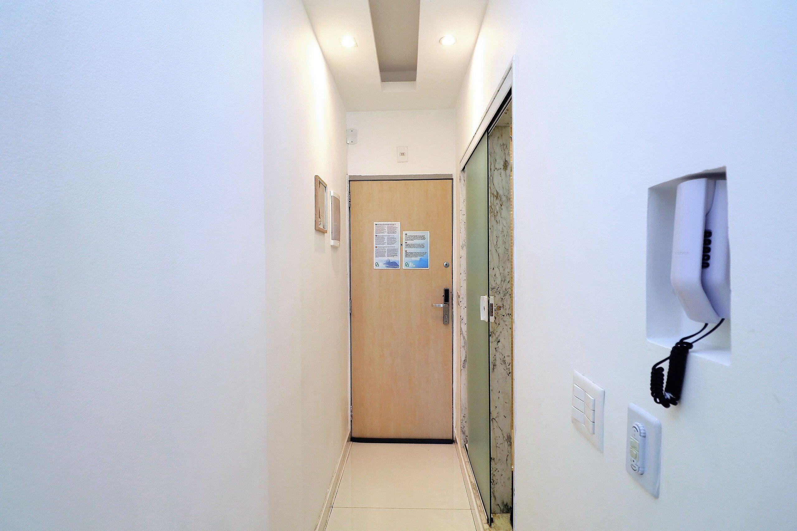 A narrow hallway with a wooden door at the end, a wall-mounted phone, and a light switch.