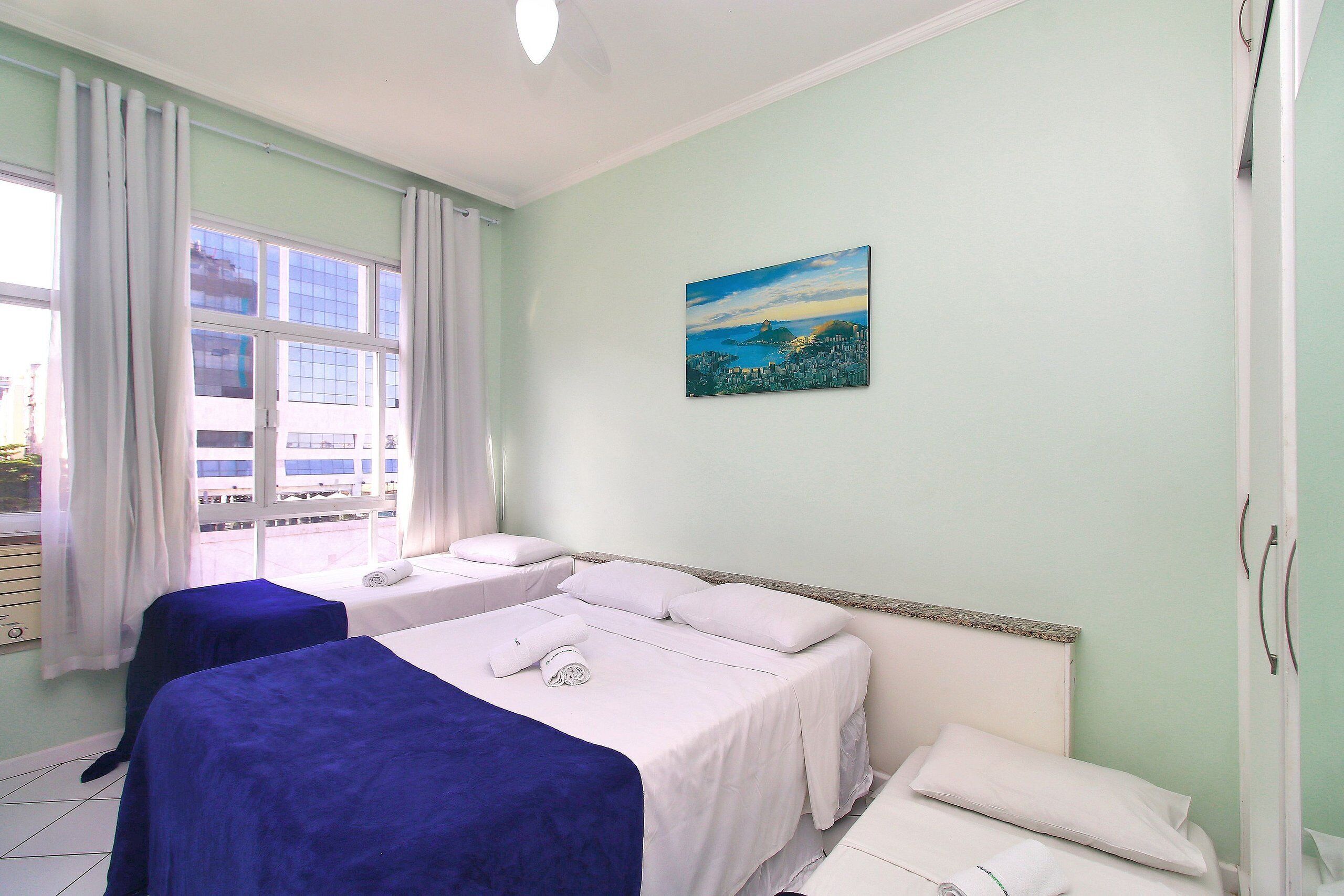 Une chambre d’hôtel avec deux lits, un tableau représentant un paysage urbain et une fenêtre avec des rideaux.