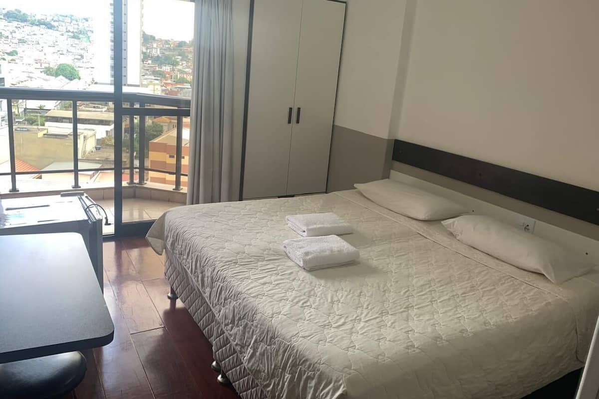 Habitación de hotel con cama, escritorio y balcón con vista a la ciudad.