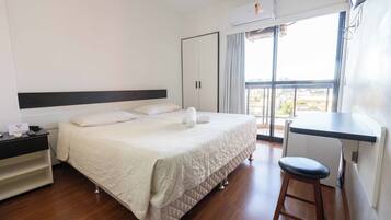 Quarto de hotel com cama, escrivaninha, cadeira, guarda-roupa e janela com vista.