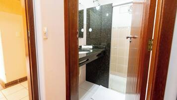Un baño con encimera negra, espejo y zona de ducha.